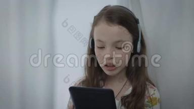 漂亮的小女孩带着耳机在平板电脑上观看<strong>音乐视频</strong>并唱歌。